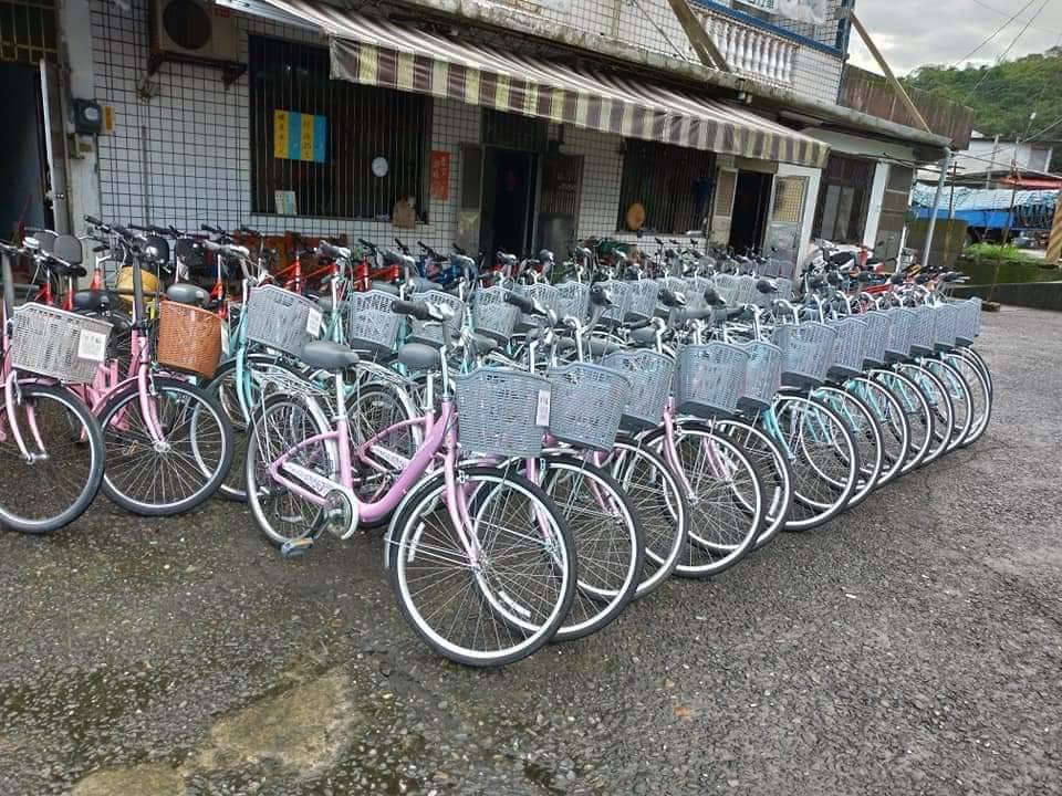 歡樂自行車店前停放多款出租單車,包含粉色和淺色單車,車上附有置物籃。
